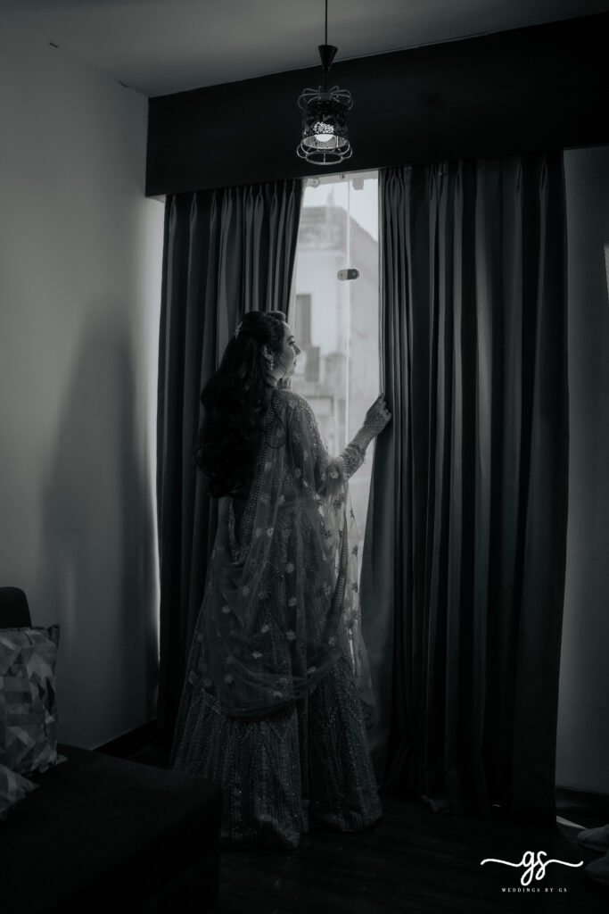 "Black and white portrait of bride looking out the window in embellished lehenga – captured before engagement ceremony by Weddings by GS"