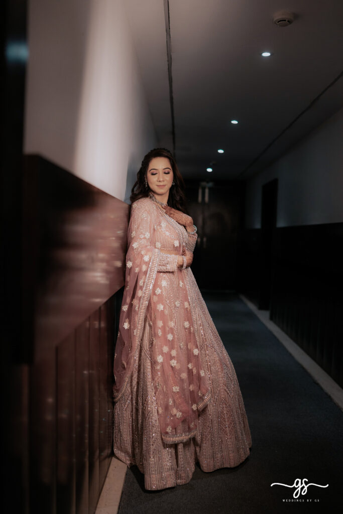 "Bride in pastel pink embellished lehenga posing gracefully before her engagement ceremony – captured by Weddings by GS"